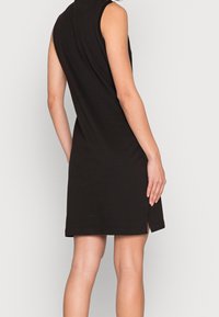 Vestito nero senza maniche con taglio dritto, spacco laterale all'orlo, texture morbida e dettagli minimi, adatto per un abbigliamento casual.