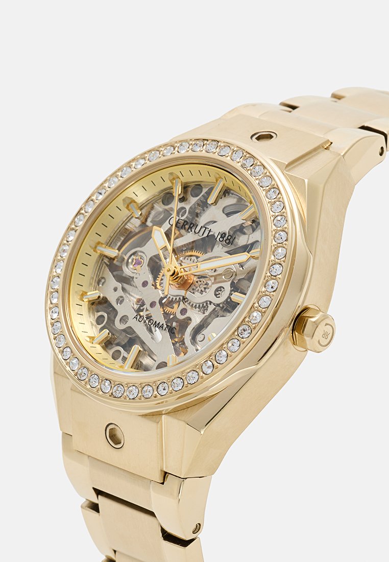 Reloj automático en tono dorado con una esfera esqueleto transparente, acentos similares a diamantes en el bisel y una pulsera de eslabones metálicos.