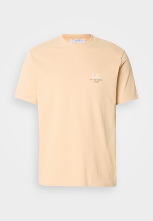 Peach-colored cotton t-shirt with short sleeves, featuring a small white graphic and text on the left chest area. Simple crew neckline.