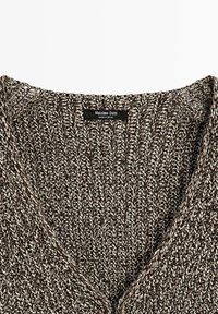 Gros plan d'un pull en maille épaisse marron et blanc avec un col en V et une étiquette noire Massimo Dutti portant la mention "Made in Spain."