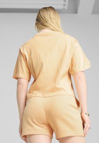 Sættet består af en ferskenfarvet bomuldst-shirt og shorts med korte ærmer, afslappet pasform og glat tekstur. Simpelt, moderne design uden mønstre.