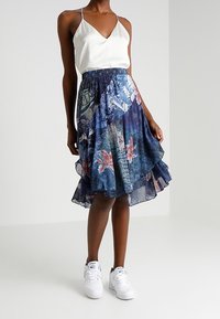 Blommönstrad kjol med volangkant i nyanser av blått och rosa, kombinerad med en vit satintopp och vita sneakers.