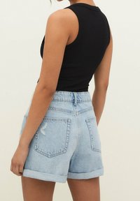 Czarny prążkowany top na ramiączkach w połączeniu z wysokim stanem, jasnoniebieskimi szortami dżinsowymi z postrzępionym dołem i podwiniętymi mankietami, widocznymi tylnymi kieszeniami.