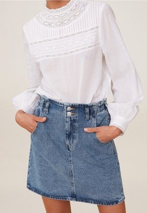 Hvid bluse med lange ærmer, blonder og læg, kombineret med en højtaljet blå denimnederdel med forlommer og dobbelte knapper.