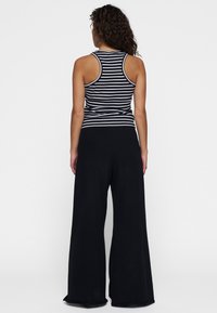Zwarte wijde broek gecombineerd met een zwart-wit gestreepte tanktop. Het materiaal lijkt zacht, met een relaxte pasvorm en racerback ontwerp.