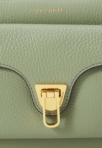 Green textured leather handbag with a triangular gold metal clasp and embossed brand name. Features edged stitching and smooth finish.