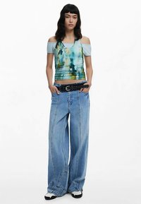 Blauw abstract patroon tanktop met off-shoulder mouwen, gecombineerd met wijde lichtblauwe jeans en een zwarte riem met studs.