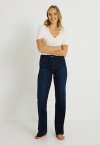 Vaqueros azul oscuro de corte recto con costuras contrastantes, cintura alta y diseño de cinco bolsillos. Combinados con una camiseta blanca ajustada de cuello en V.