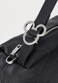 Manico di borsa in pelle nera con texture, accentuato da un hardware a forma di Topolino in argento e chiusura con zip. Dettagli cuciti sul manico.