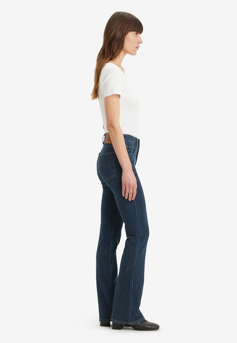 Jeans évasés à rayures bleu foncé avec une finition texturée, dotés d'une taille mi-haute et de poches arrière, assortis d'un haut ajusté blanc.