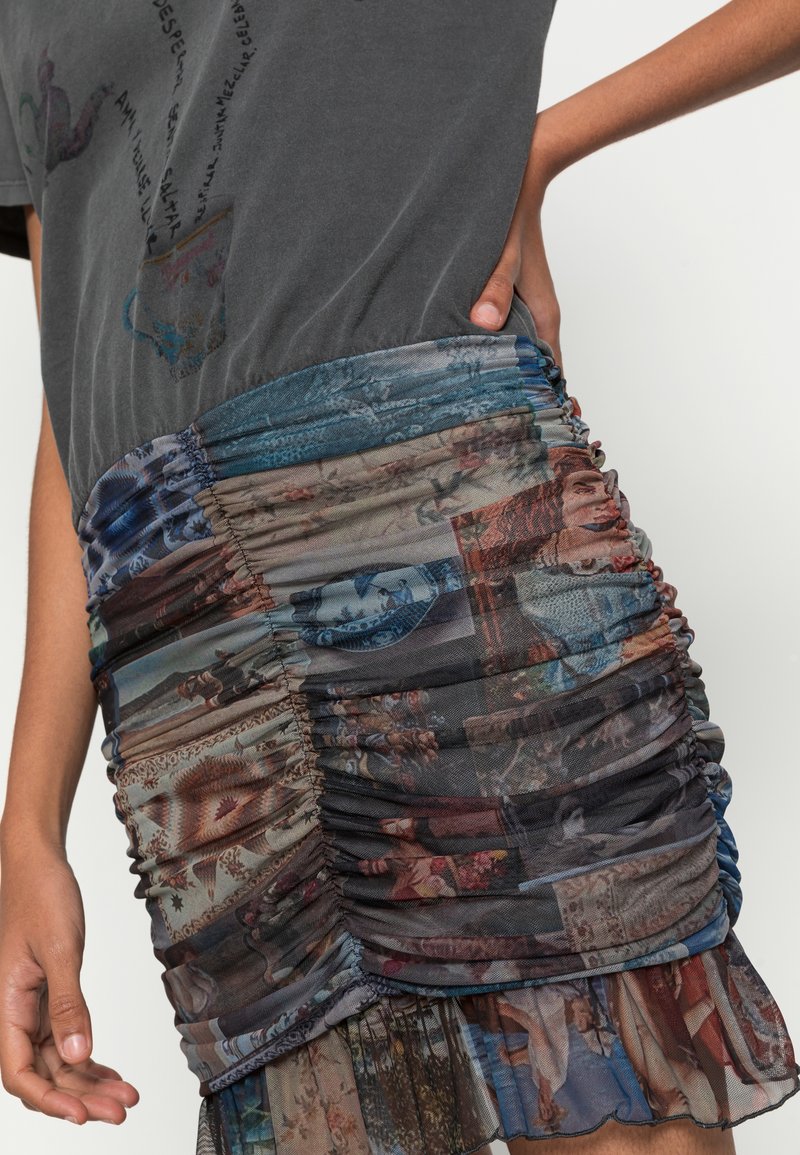 Szara koszulka z grafiką, zestawiona z wielokolorową mini spódnicą z marszczeniami, na której znajdują się różnorodne obrazy i wzory. Miękka tkanina, luźny krój.
