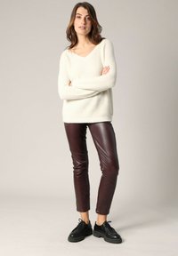 Pull en maille texturée blanc cassé avec un col en V, associé à un pantalon en simili cuir bourgogne profond et des chaussures noires à lacets. Design simple et ajusté.