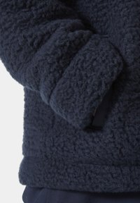 Granatowa polarowa kurtka z teksturowaną, pluszową powierzchnią i kieszenią po boku. Posiada luźny krój oraz mankiety na rękawach.