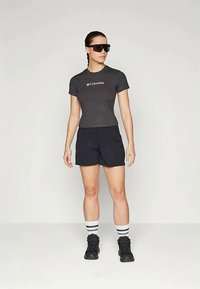 Grå tettsittende T-skjorte med Columbia-logo, kombinert med marineblå shorts. Modellen har på seg svarte solbriller, svarte sko og stripete hvite sokker.