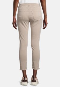 Jeans beiges courts avec ourlet effiloché, design à cinq poches et coupe ajustée. Portés avec des baskets épaisses de couleur claire.