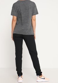 Šedé tričko s krátkým rukávem v kombinaci s černými úzkými kalhotami. Tento outfit se vyznačuje měkkou tkaninou, uvolněným střihem a je doplněn světlými teniskami.