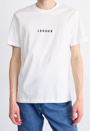 Bílý bavlněný tričko s centrálním černým potiskem "JORDAN". Krátké rukávy, kulatý výstřih a volný střih. Textura vypadá hladce.