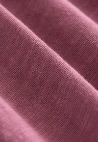Zacht, gestructureerd stoffen in een gedempt roze kleur, met een fijn breipatroon dat subtiele variaties in dikte vertoont en lichte pillen zichtbaar zijn.