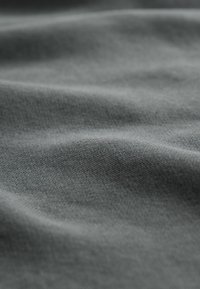 Tissu gris doux avec un tissage texturé subtil et de légants plis créant une surface lisse et fluide.