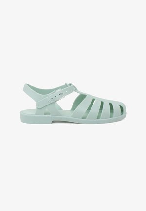 Sandalias de plástico verde claro con diseño de cortes, tira en el tobillo, hebilla ajustable y suela plana. Adecuadas para climas cálidos.