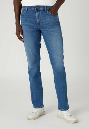 Jeans in denim blu con design a gamba dritta, leggero effetto scolorito e classico stile a cinque tasche. Indossati con sneakers bianche.