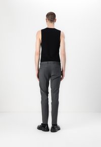 Fekete ujjatlan blúz és szürke, slim fit szabású nadrág. A fényes fekete cipők kontrasztot alkotnak a nadrág matt anyagával.