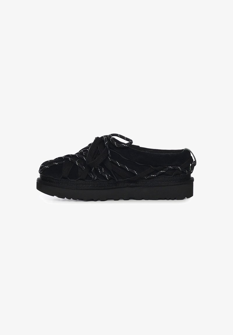 Sandalia casual negra con suela gruesa y múltiples correas cruzadas de estilo cuerda que cubren el dedo del pie descubierto y los lados.