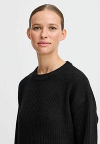 Svart ribbad stickad tröja med rundad halsringning och långa ärmar. Texturen är mjuk och passformen är avslappnad. Enkelt, klassisk design.