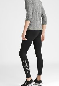 Leggings sportivi neri realizzati in un tessuto elasticizzato, con un design aderente e un logo grigio ben visibile lungo la gamba sinistra.