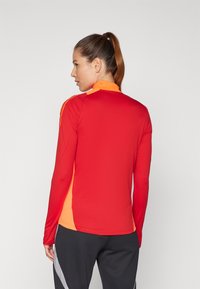 Langärmliges Sportoberteil mit einem roten Körper und orangefarbenen Akzenten am Kragen und an den Seiten. Glattes, dehnbares Material mit einer figurbetonten Passform.