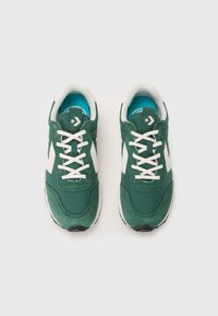 Zapatilla verde con acentos blancos, tela texturizada y suela de goma. Cuenta con cordones, cuello acolchado y logo en la lengua.