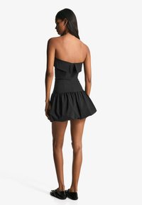 Rochie neagră fără bretele, cu corsaj mulat, detalii cu volane în partea de sus și fustă evazată. Închidere cu fermoar la spate.