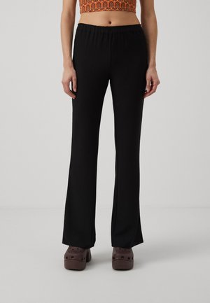 Black flared pants with an elastic waistband, crafted from textured fabric, paired with brown platform clogs on a neutral background.