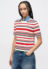 Πλεκτό ριγέ πουλόβερ σε κόκκινο, λευκό και ναυτικό μπλε, με κοντά μανίκια και πουκάμισο από τζιν με γιακά από κάτω. Χαλαρή εφαρμογή.