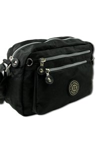 Black fabric crossbody bag with two front zippered pockets, silver hardware, and a circular logo patch on the side. Textured surface.