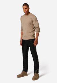 Beige longsleeve shirt gecombineerd met zwarte leren broek en tan laarzen. Het shirt heeft geribbelde mouwen; de broek heeft textuuraccenten op de knieën.