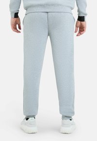 Grijze sweatpants van zacht materiaal met taps toelopende pijpen, voorzien van zwarte accenten op de boorden en de zijzakken. Gepaard met witte sneakers.