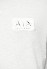 Λευκό βαμβακερό T-shirt με ανάγλυφο, ορθογώνιο λογότυπο που φέρει το “A|X” και “ARMANI EXCHANGE” ανάγλυφα σε ασημί χρώμα. Λείο υφαντό.