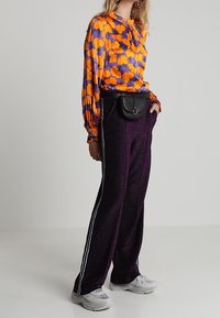 Färgglad långärmad blus med orange och lila blommönster, kombinerad med svarta högmidjade tapered-byxor med vita sidostripes.