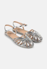 Silberne metallische Riemchensandalen mit offenem Zehenbereich, ausgestattet mit überkreuzten Riemen und verstellbarem Knöchelverschluss; glatte flache Sohle.