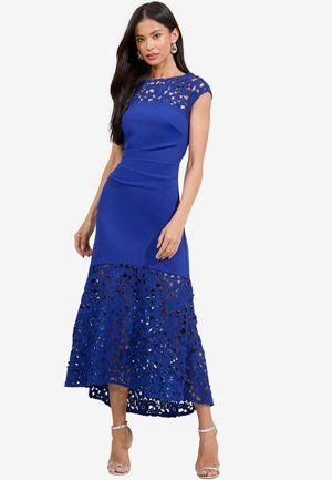 Robe bleue avec un corsage en dentelle et un ourlet évasé en dentelle découpée de manière complexe. Présente une silhouette ajustée et un design longueur genou.