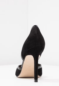 Chaussure à talon haut en daim noir avec un bout pointu, des accents noirs brillants au talon et à la bride, et un intérieur beige lisse. Taille 37.