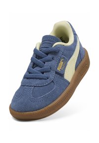 Blå mockaskor med beige detaljer, rund tå, snörningar och en strukturerad brun gummisula. Har en gyllene logotyp på sidan.