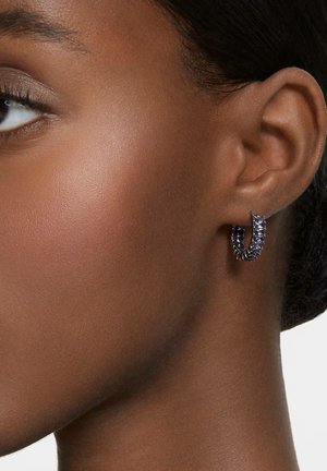 Silberner Creolen-Ohrring mit strukturiertem, gedrehtem Design und dunklen Akzenten. Der Hautton des Modells ist ein sattes Braun, das den Kontrast des Ohrrings hervorhebt.