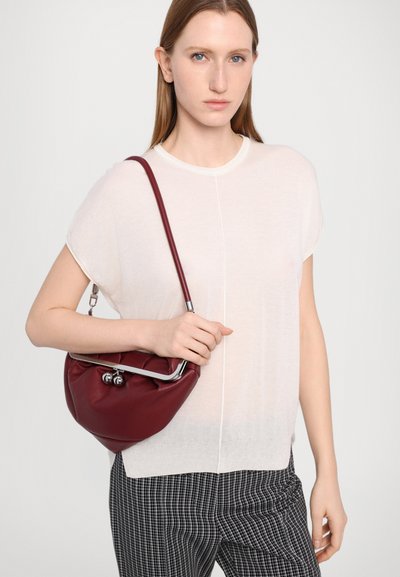 Burgundy leather handbag with a metal frame and rounded shape, featuring a smooth texture and silver accents, carried with a light top and checked pants.