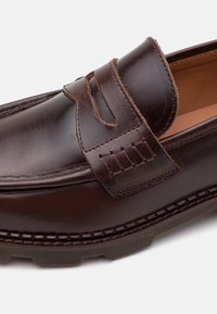 Barna bőr loaferek, varrott részletekkel, slip-on kialakítással és texturált talppal. Díszítő pánt található a lábfej részen.