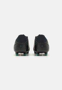 Svart fotballsko med teksturert mønster, lav design og grønne knotter. Har en glatt syntetisk overdel og polstret krage.
