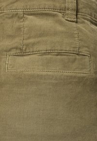 Khaki corduroy stof met verticale ribbels. Voorzien van een patchzak aan de achterkant met subtiele stikdetails. Zachte textuur en fletse kleur.