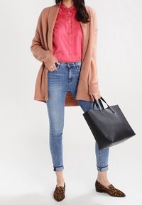 Hellbeige Cardigan über einem rot gestreiften Hemd mit Knöpfen, kombiniert mit blauen Skinny-Jeans, braunen Leo-Print-Schuhen und einer schwarzen Tote-Bag.