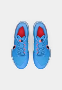 Ζευγάρι μπλε αθλητικά παπούτσια με μαύρα και πορτοκαλί λογότυπα Nike, γκρι σόλες και κόκκινη εσωτερική επένδυση, εμφανιζόμενα από πάνω σε λευκό φόντο.